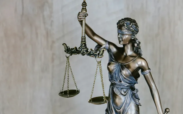 Estatua de la Justicia con los ojos vendados y balanza sobre fondo claro